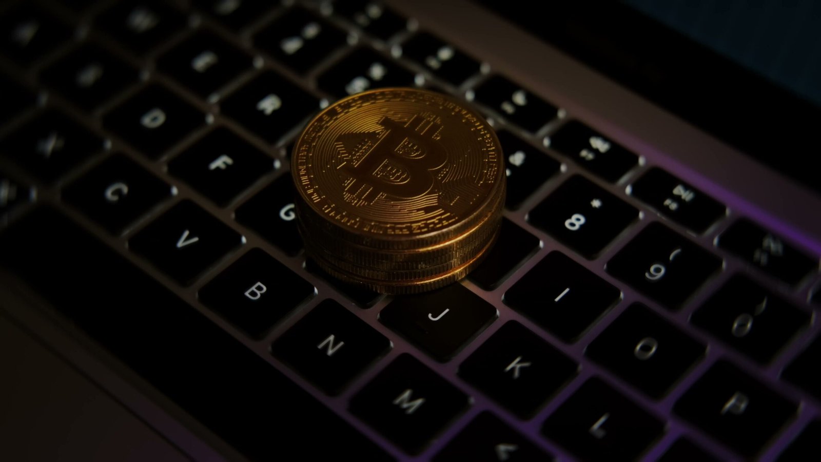 Bitcoin coin on computer keyboard with purple lighting